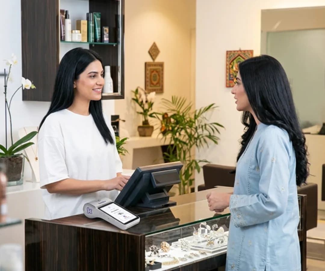Beauty salon staff member serving a client at a busy reception counter