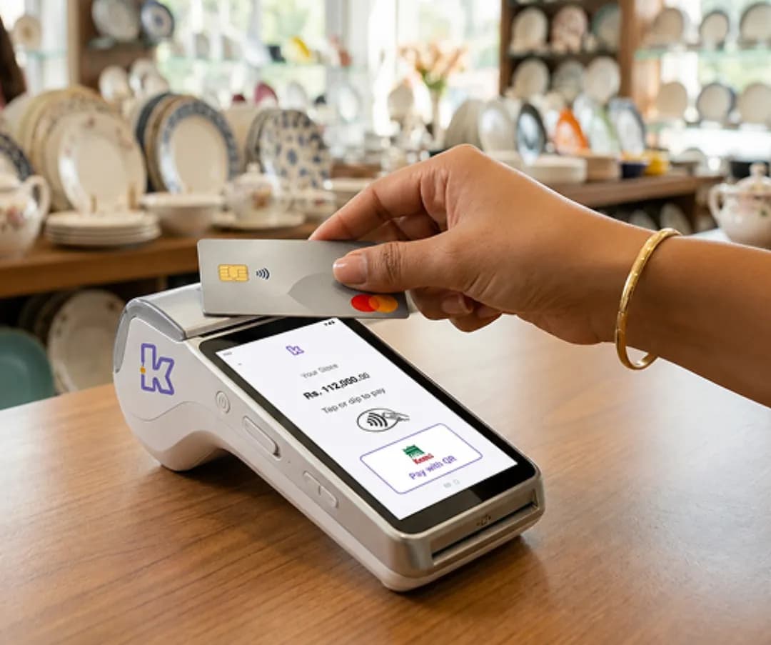Shop worker handing a Keenu payment terminal to a customer at the checkout counter
