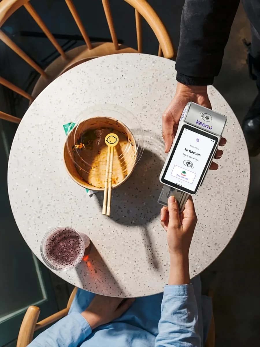Customer paying on a Keenu terminal at a cafe table with a coffee
